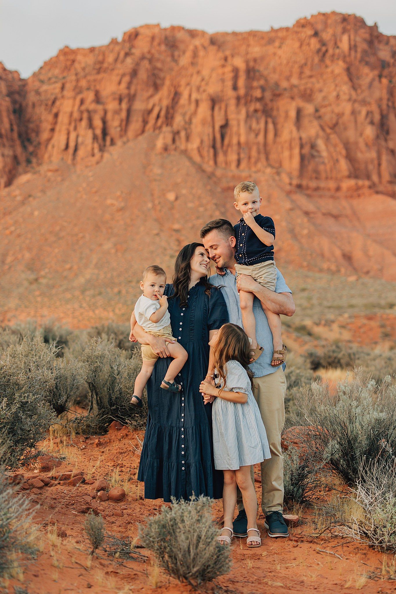 Family of five posing in red rock desert landscape with dramatic sandstone buttes at golden hour.