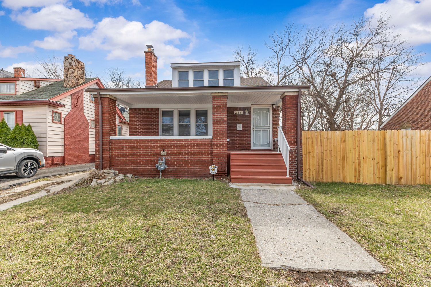 Classic white clapboard bungalow with covered front porch, brick accent wall, and detached garage on a corner lot.