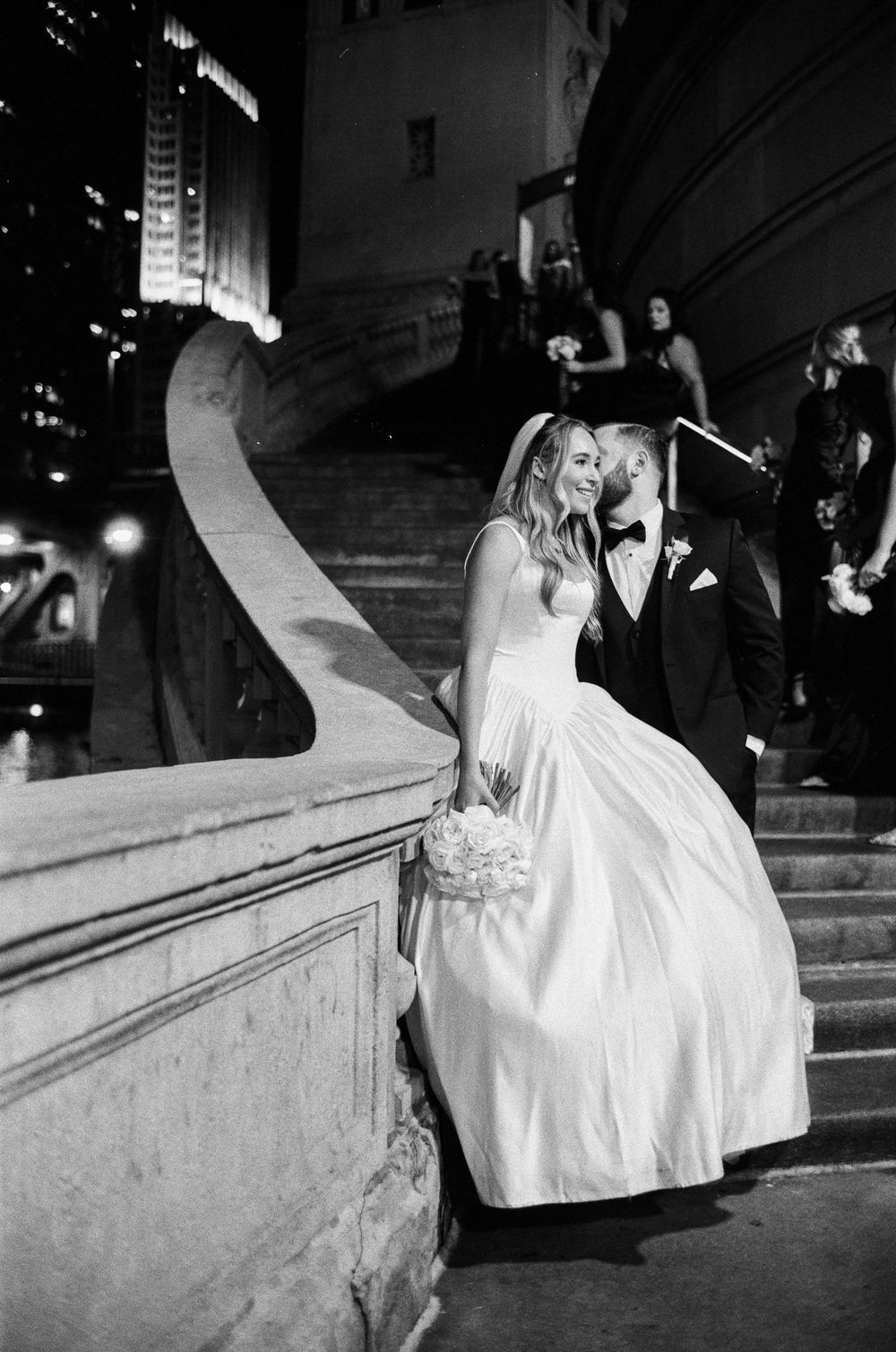 Black and white 35mm film photo of a bride and groom sharing a romantic moment on grand stone steps at night in downtown Chicago.