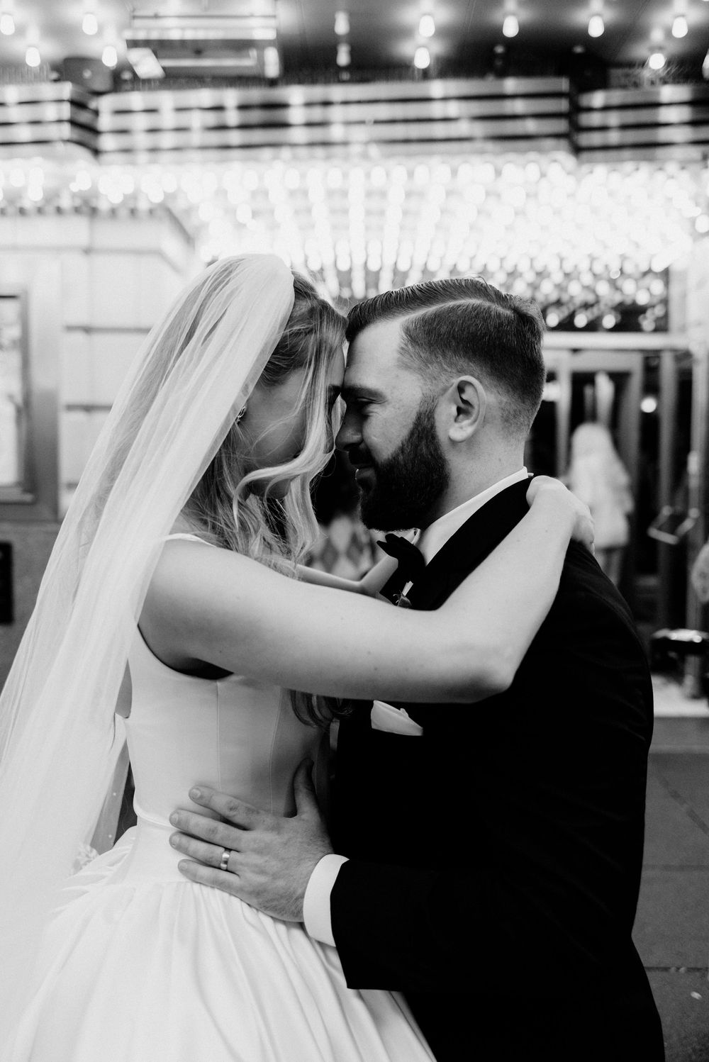 Black and white photo of a bride and groom sharing an intimate moment, touching foreheads under the Chicago Theater's Marquee lights.