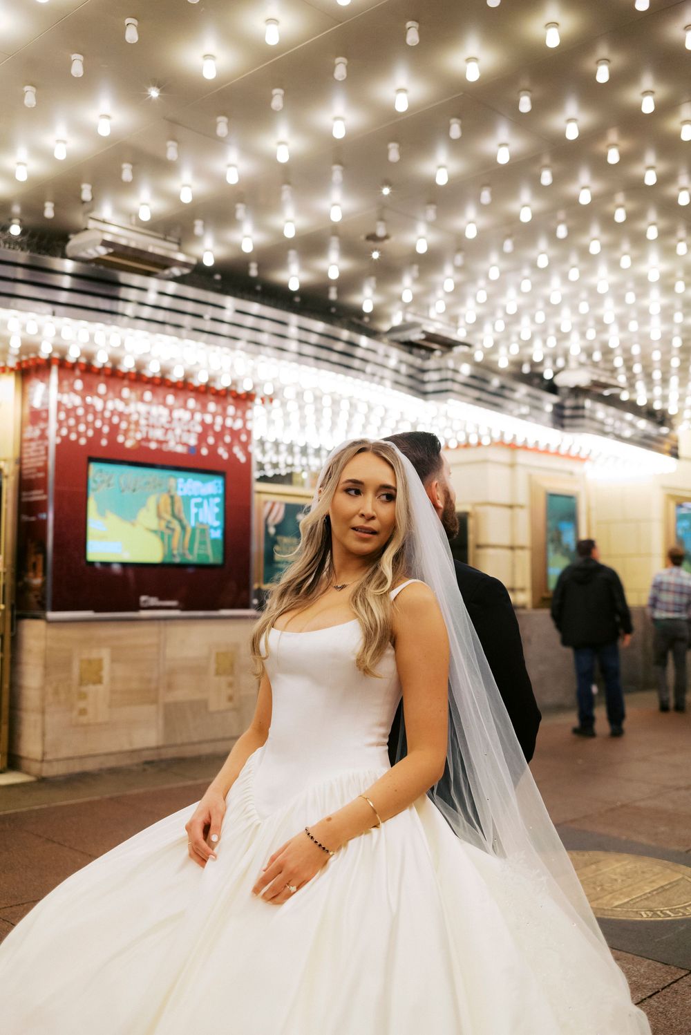 Beautiful bride in white ball gown with veil posing under The Chicago Theater marquee lights.
