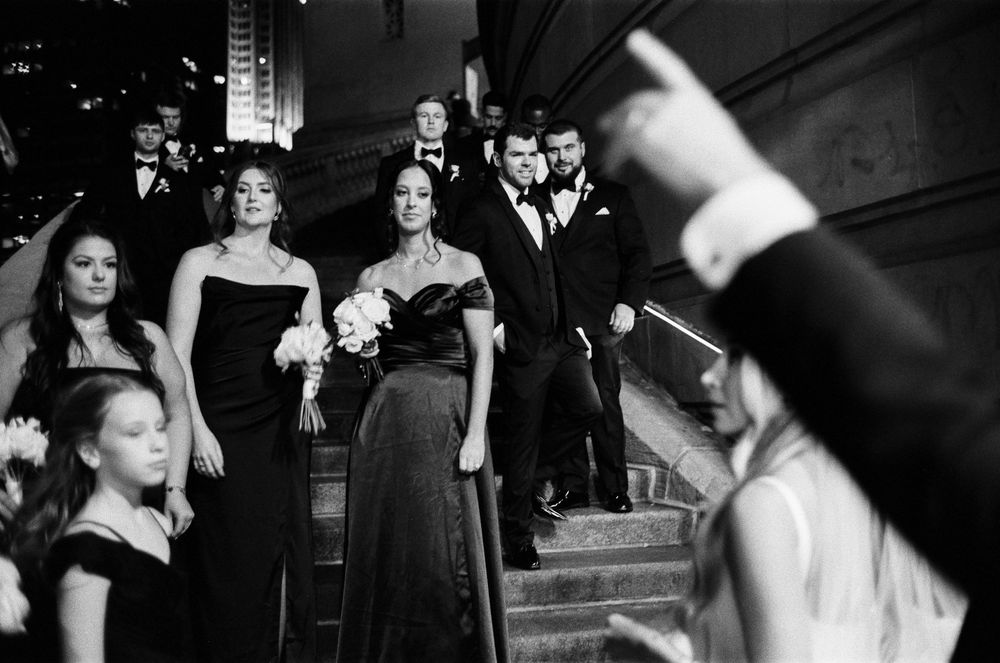 Bridesmaids in dark gowns and groomsmen descend Chicago riverwalk staircase in photojournalistic black and white tones.