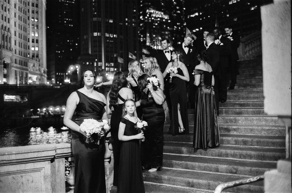 Black and white photo of elegantly dressed wedding party on Chicago city steps at night with bouquets.