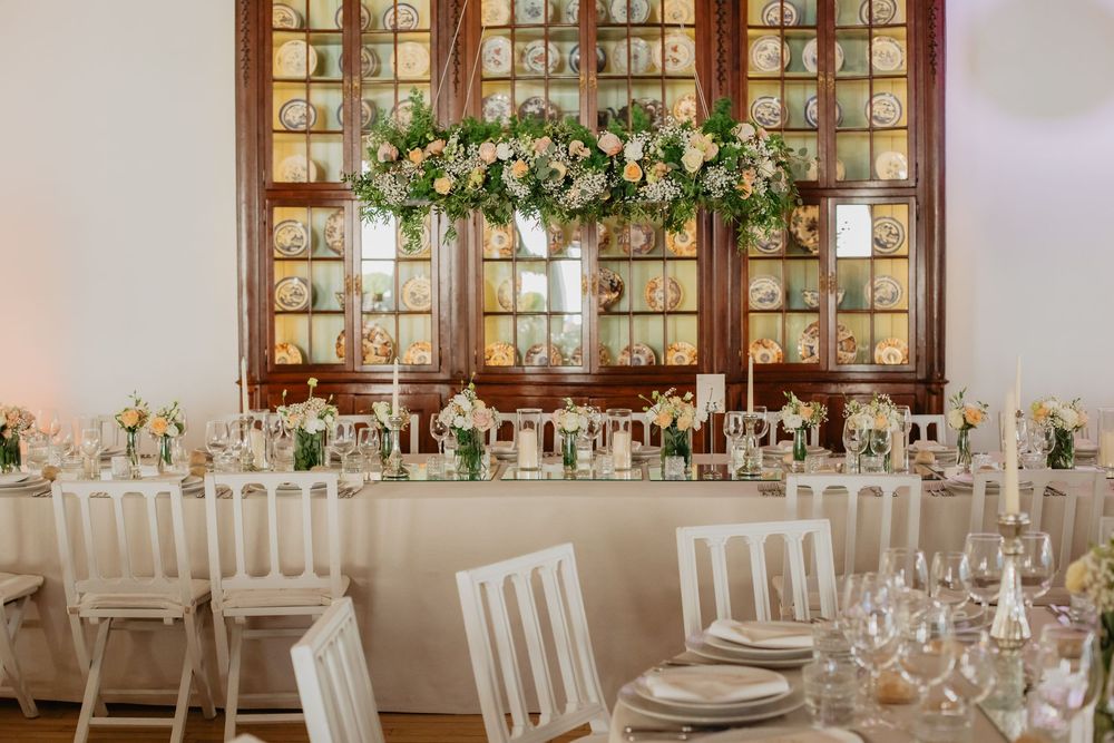 Elegant wedding reception with white chairs, floral centerpieces, and a grand flower arrangement above the head table.