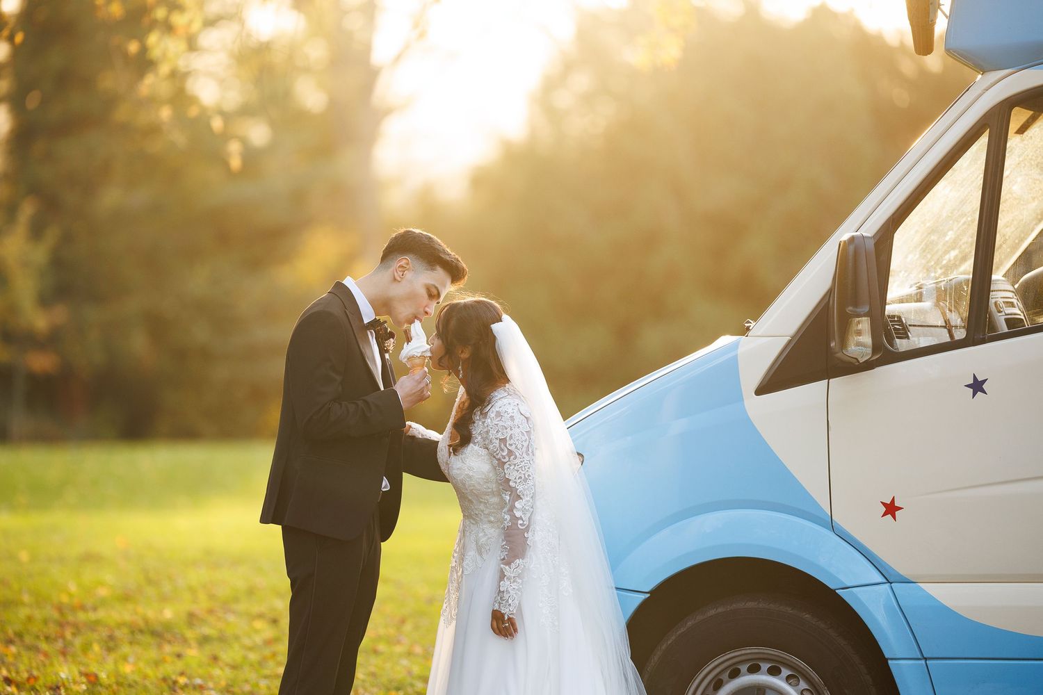 A bride and groom hold hands walking through a city square, she in a lace gown, he in a black tuxedo.