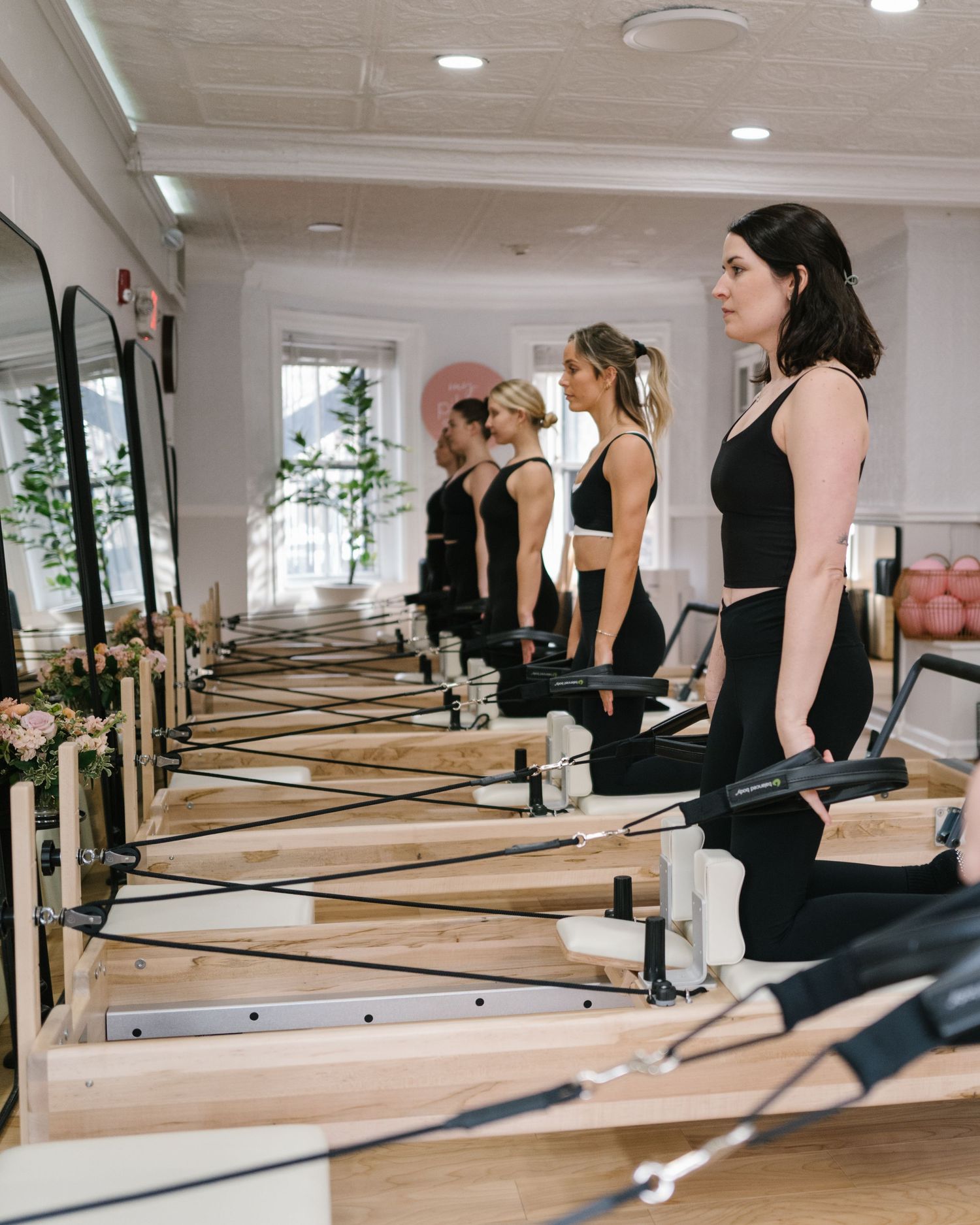 Women in black activewear practicing Pilates on reformer machines in a bright, elegant studio with mirrors.