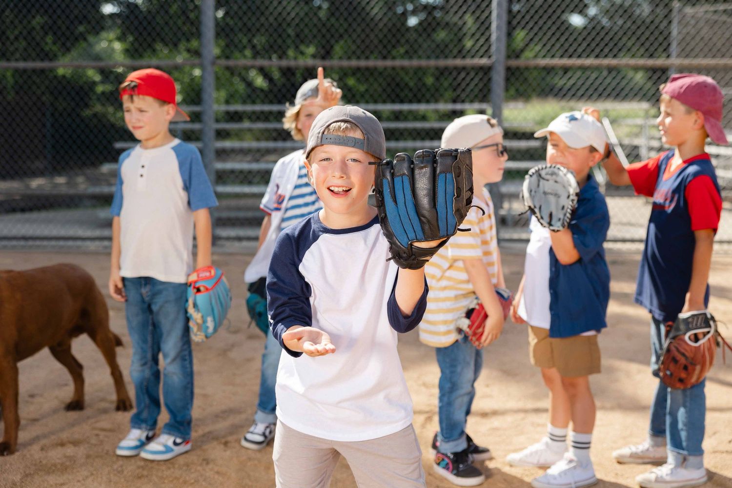 Young boys in baseball uniforms smiling and holding gloves on a baseball field during a youth league game.