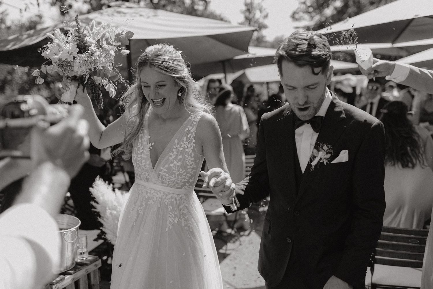 A black and white wedding photo showing a couple walking together outdoors at a daytime celebration.
