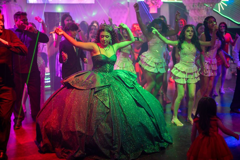 Young woman in green ballgown dancing at a vibrant quinceañera party with colorful neon lights.