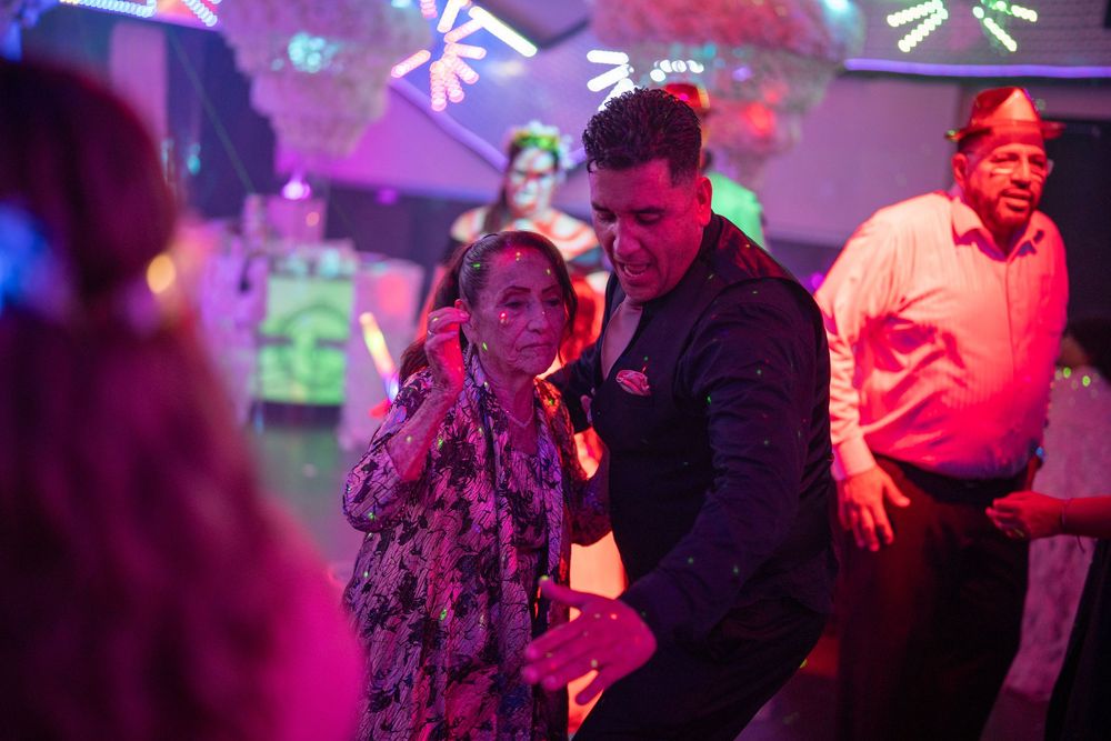 Two people dancing together at a vibrant neon-lit party with colorful stage lights in the background.