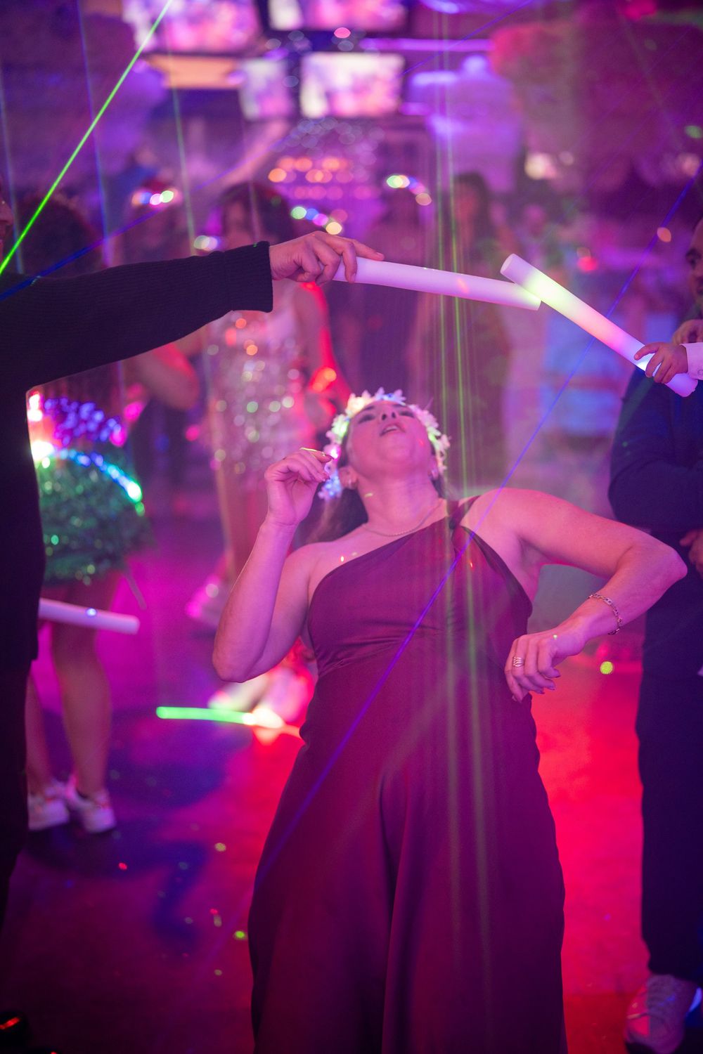 Woman in dark gown dancing at a vibrant nightclub with glowing neon lights and glow sticks.