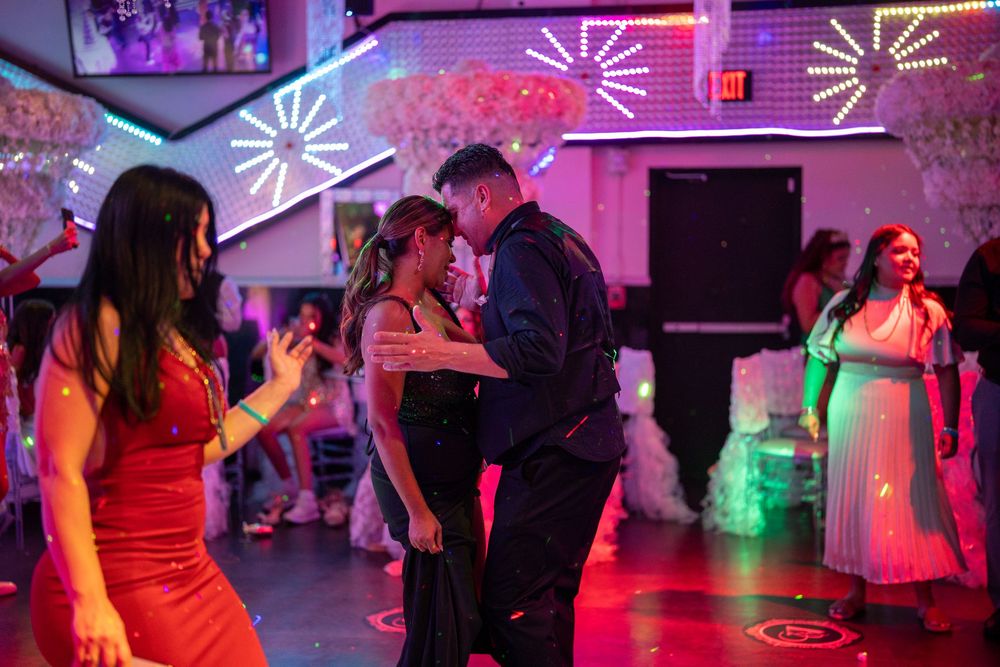 Couples dancing under colorful neon lights at a festive indoor dance party or prom event.