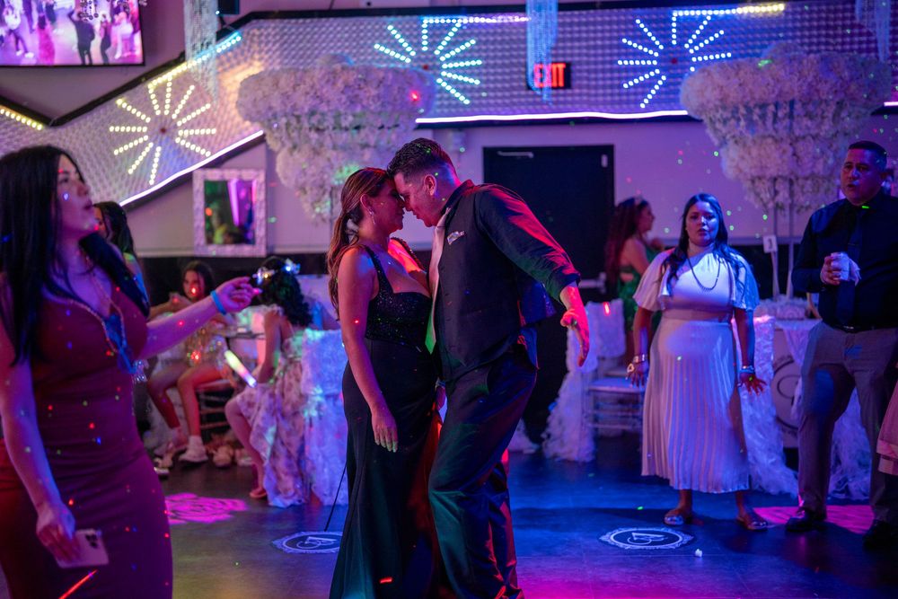 Couple dancing closely at a vibrant prom or wedding reception with colorful purple and blue lights.
