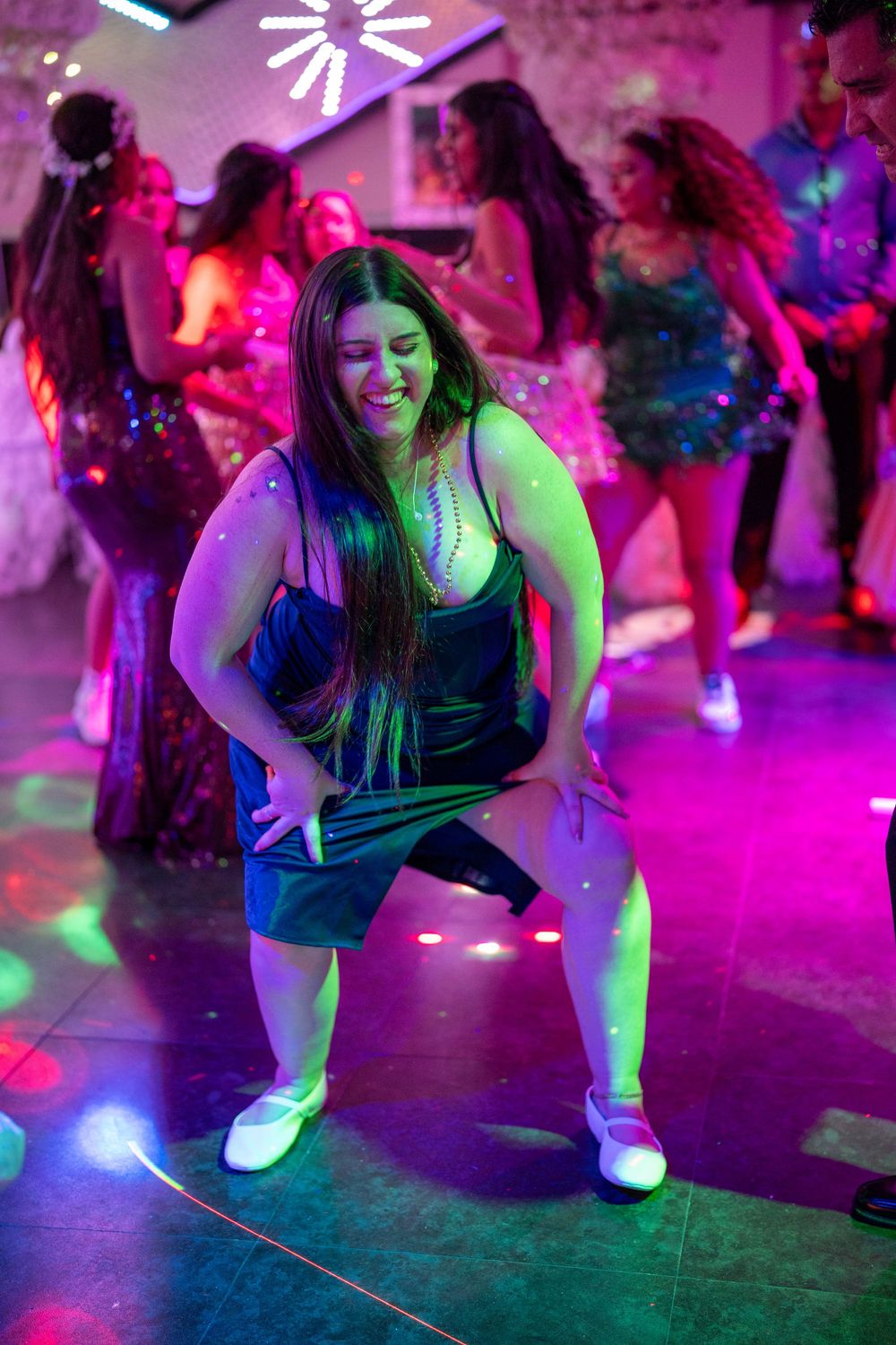 Woman dancing energetically on a colorful lit dance floor at a nightclub party with other dancers in background.