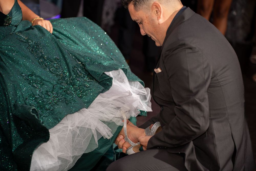 Man in black suit adjusting green sparkly gown with white tulle detail at formal event.
