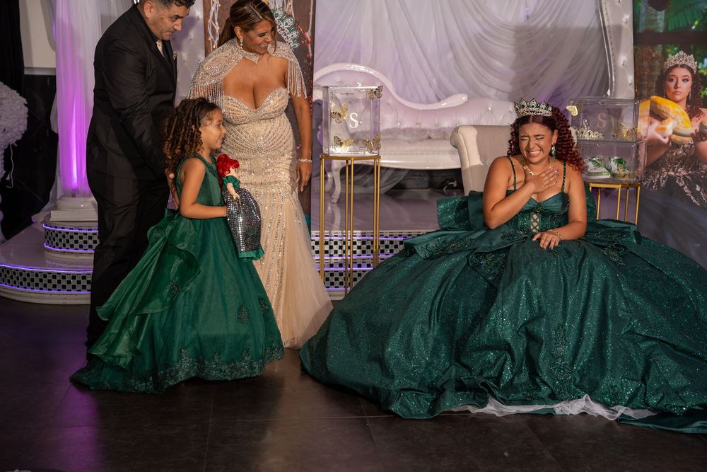 A young girl and quinceañera in matching emerald green ball gowns celebrate together on a decorated stage.
