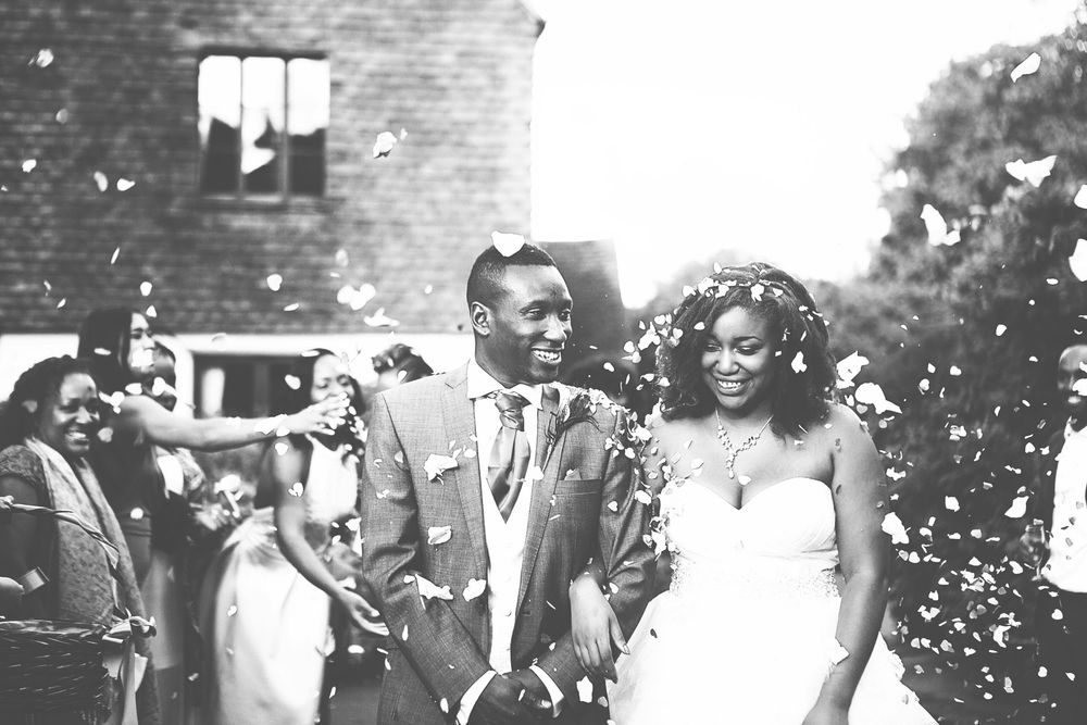 Black and white photo of a joyful newlywed couple walking through confetti at their outdoor wedding ceremony.