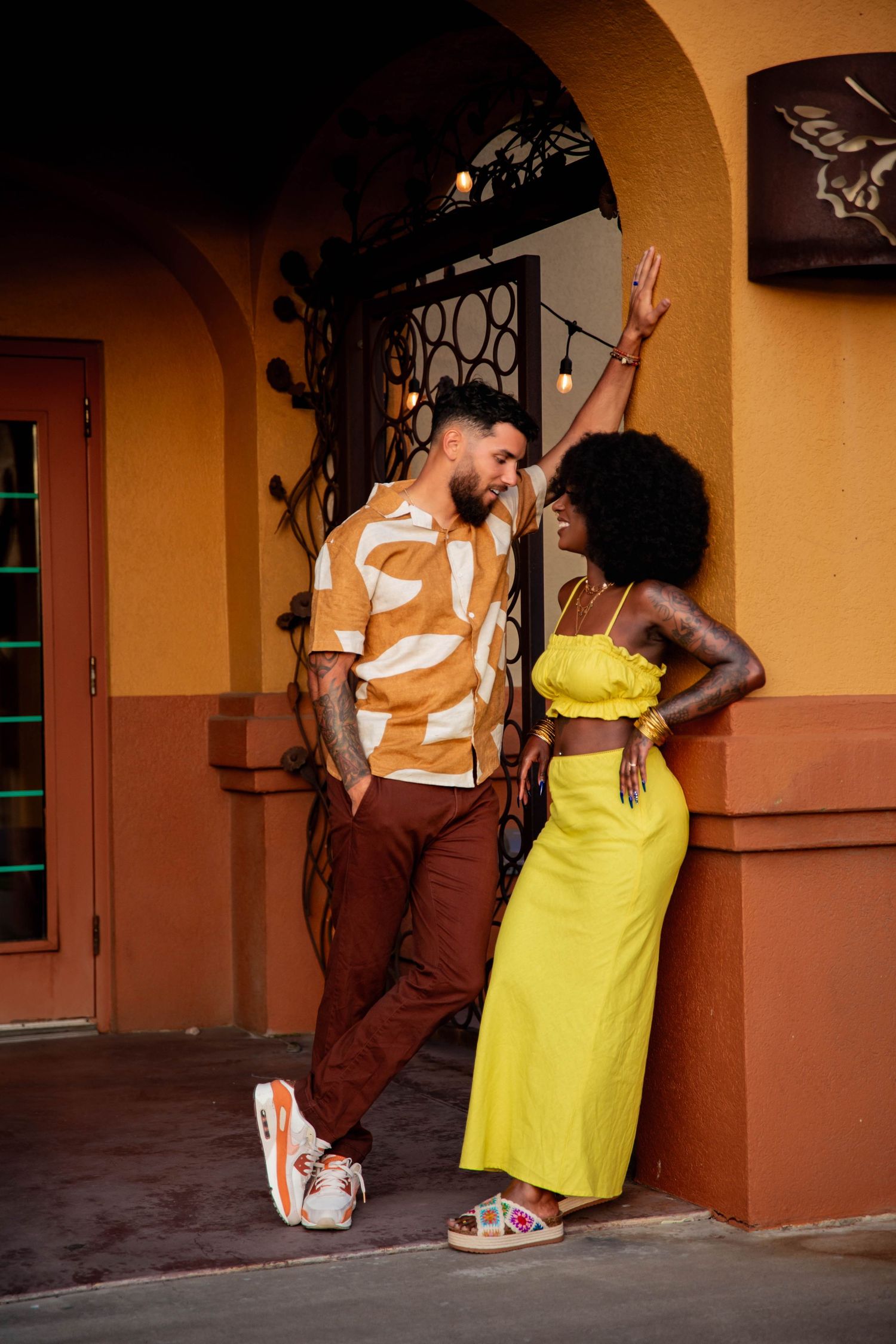 A couple in brown and yellow outfits against an orange wall. mixed couple  best photographer in southern utah