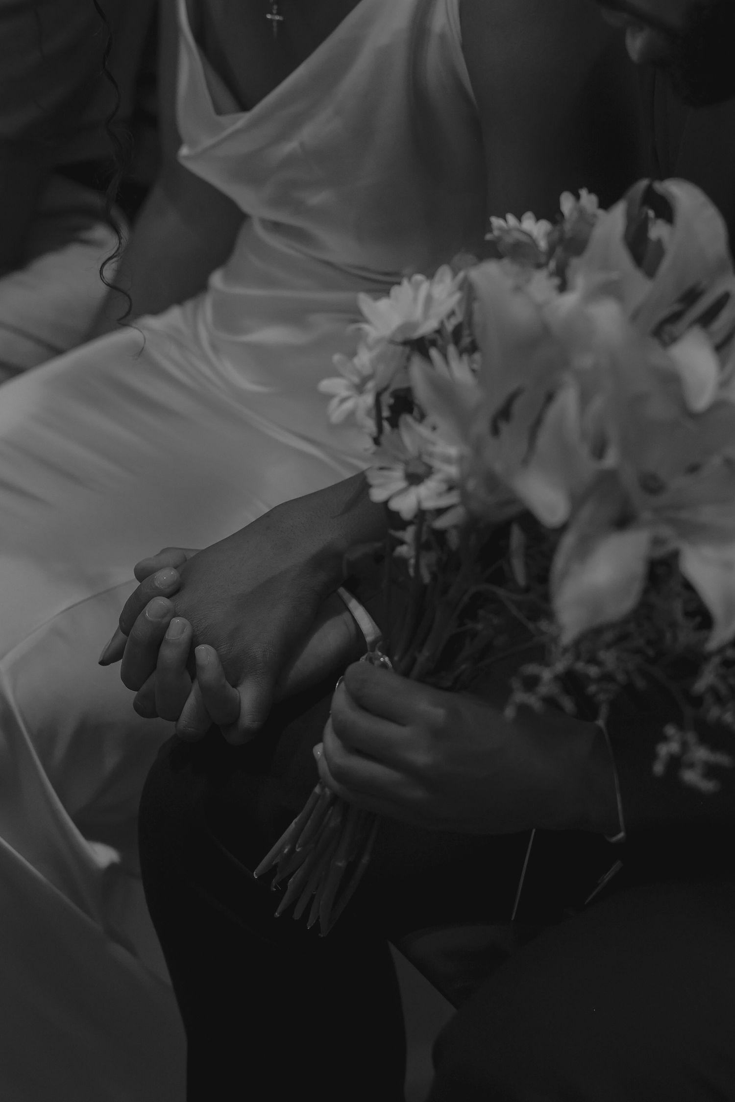Black and white photo of bride and groom holding hands and a floral bouquet at a wedding ceremony.