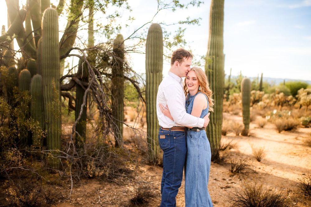Couple embracing tenderly among tall saguaro cacti in the Arizona desert during golden hour.