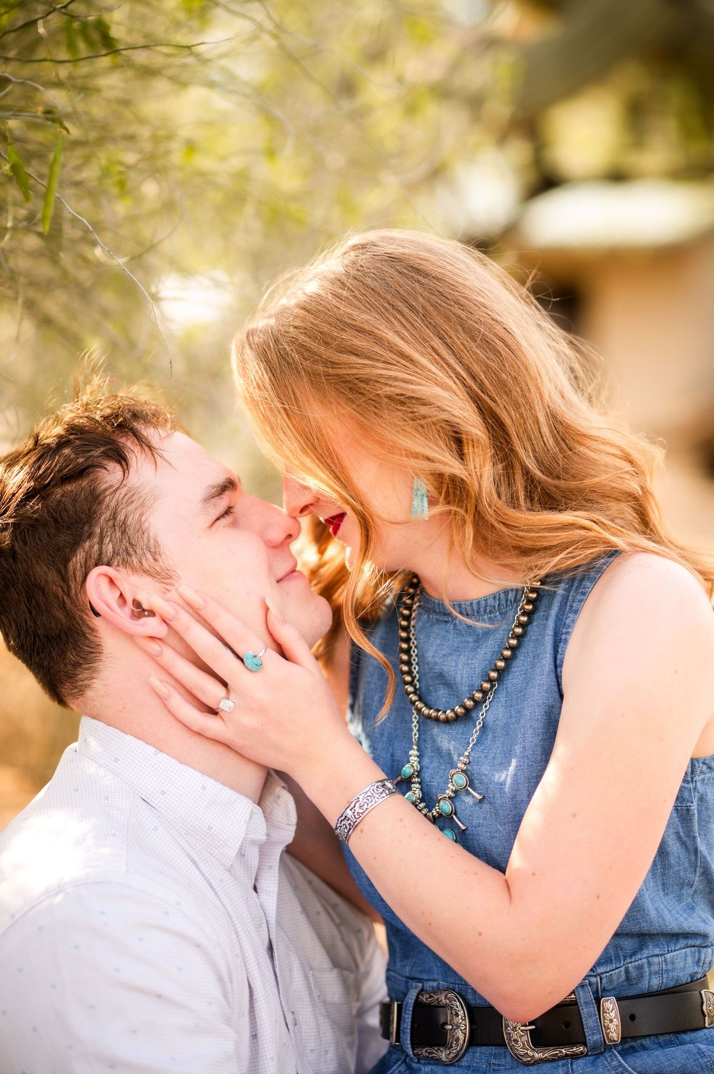 Close-up of a young couple about to kiss outdoors, woman wearing turquoise jewelry and denim dress.