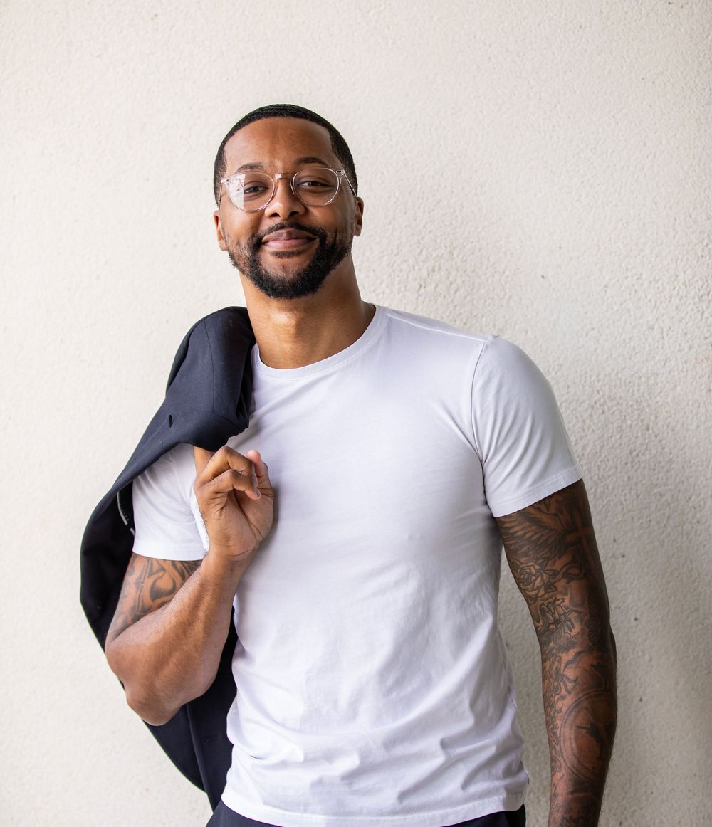 Professional portrait of man in white t-shirt holding jacket against white background.