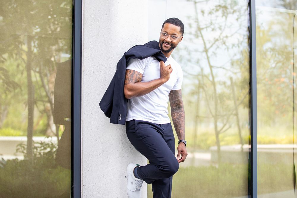 Man in casual attire poses playfully against modern building exterior.