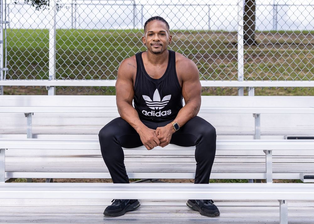 Athletic person in Adidas tank top sitting on bleachers at outdoor sports facility.