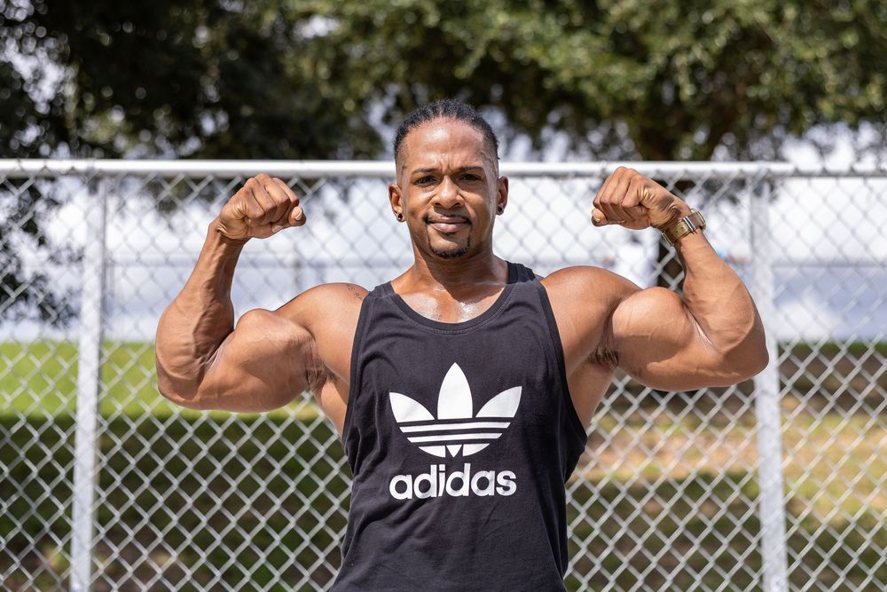 Strong athlete in black Adidas tank top flexing muscles outdoors.
