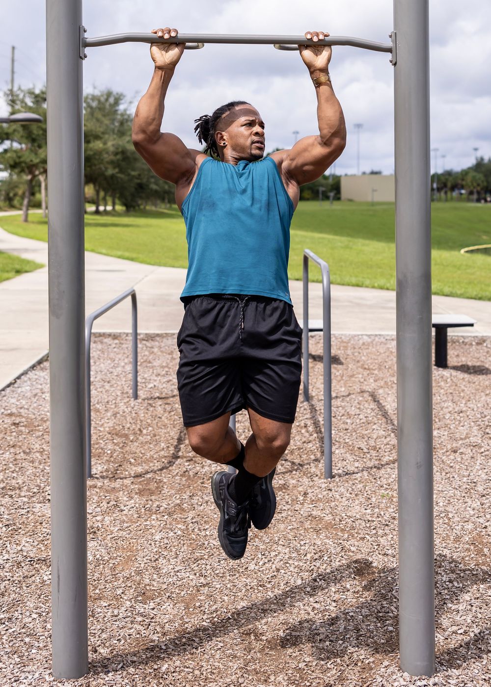 Athletic person performing pull-ups on outdoor exercise equipment wearing teal tank top.