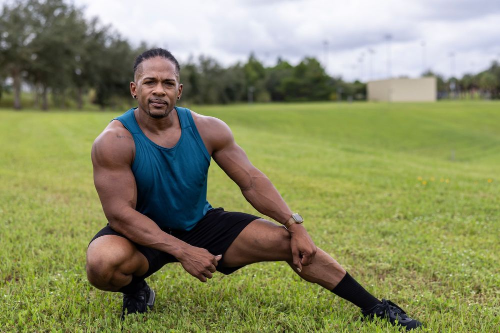 Athletic person in teal tank top and shorts stretching on grass field.