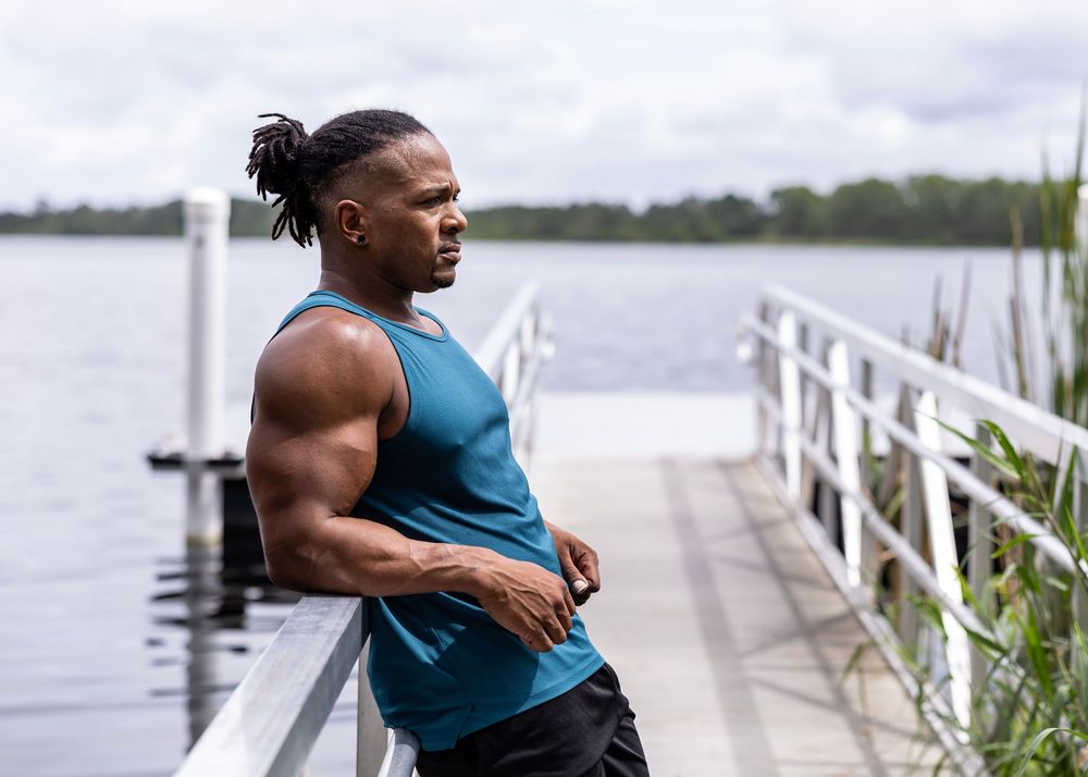 Athletic person in teal tank top standing on dock overlooking waterfront.