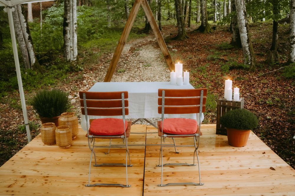 Two red chairs on a wooden deck with candles and an arch in a serene forest wedding setting.