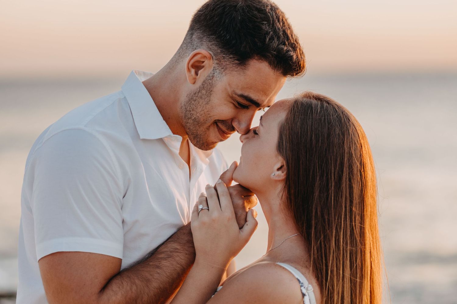 Romantic couple sharing an intimate moment at sunset by the ocean, touching foreheads and holding hands at Arashi beach aruba