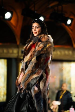 Model poses on runway wearing a luxurious multicolored striped fur coat while carrying a black handbag.