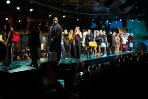 Fashion show finale with diverse models on runway in colorful outfits before seated audience.