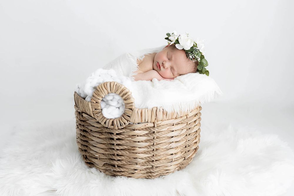 Newborn baby sleeping in wicker basket with white fur, wrapped in white by Menifee family and newborn photographer.