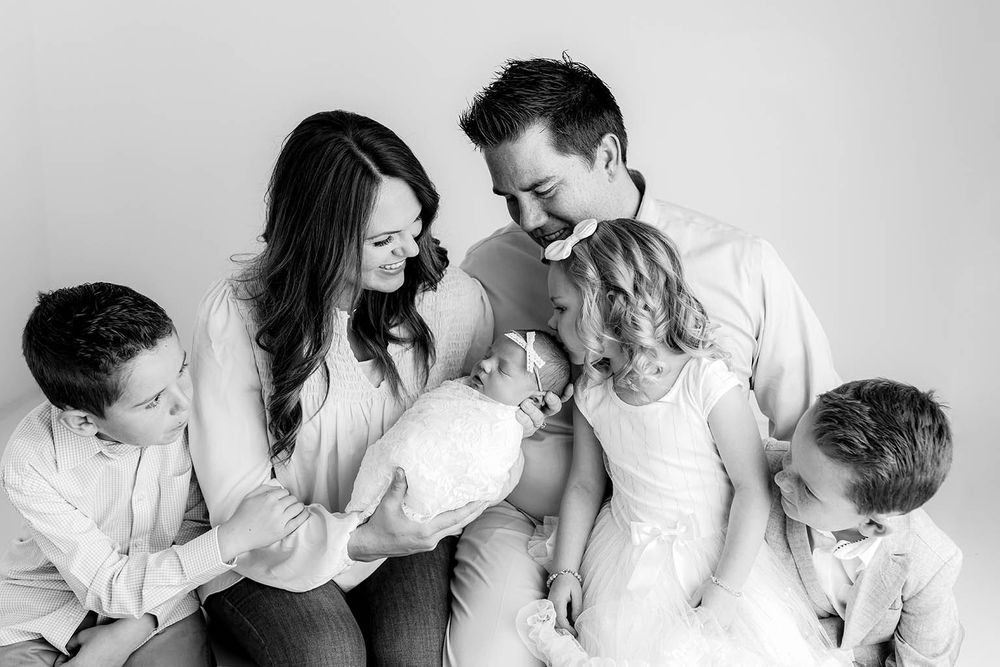 Black and white family portrait of parents and three children lovingly gathered around new baby by Menifee family and newborn photographer.