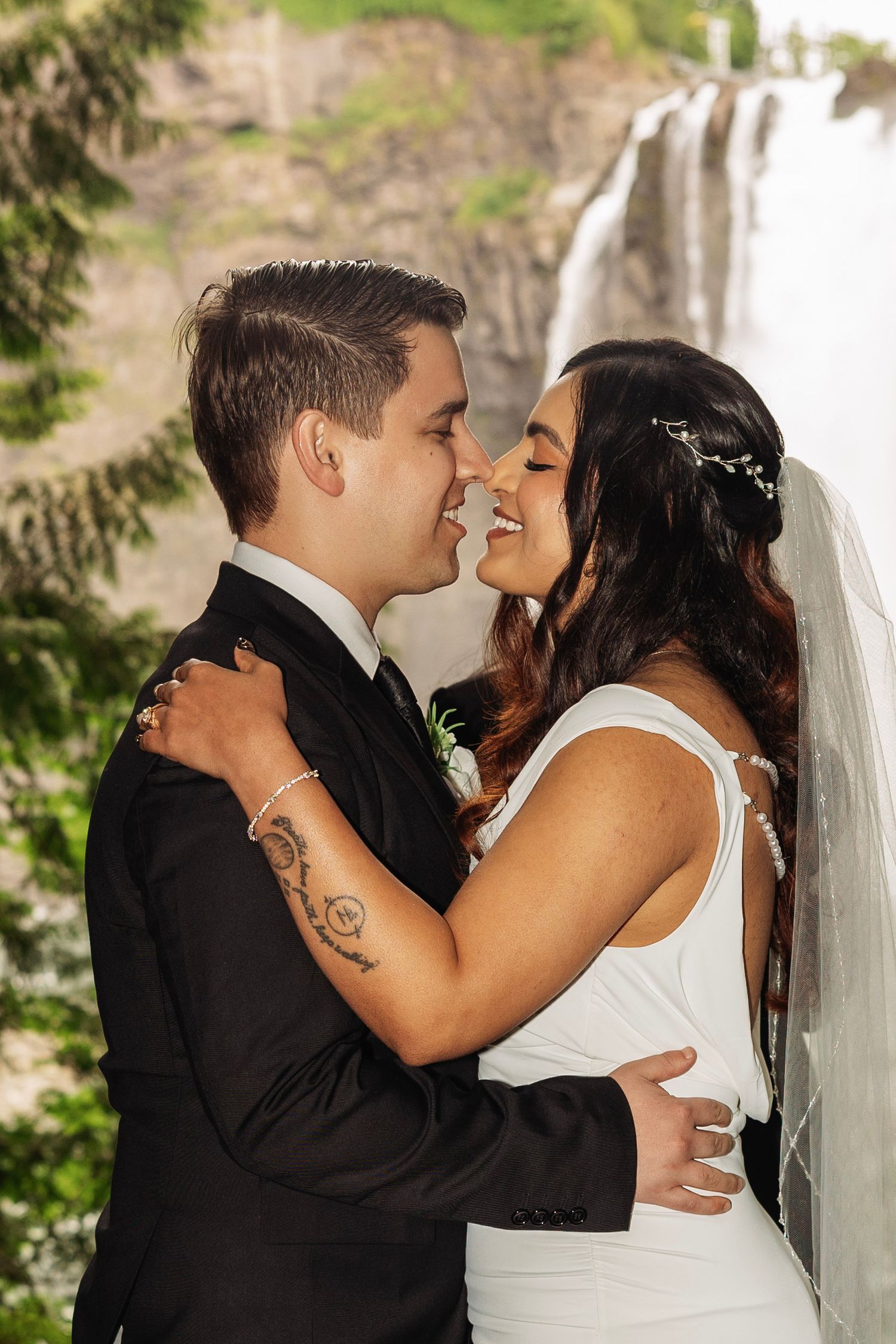 Bride and groom pose on a forest path surrounded by lush green ferns, bride holding a white bouquet.