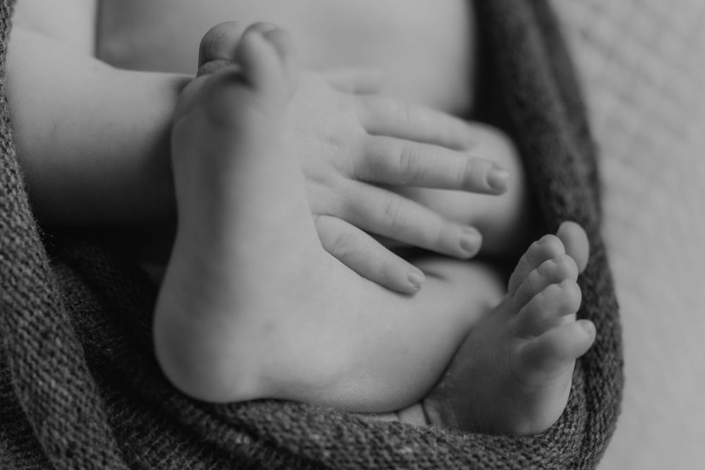 Black and white close-up photo of a newborn baby's tiny feet and hand wrapped in a soft knit blanket.