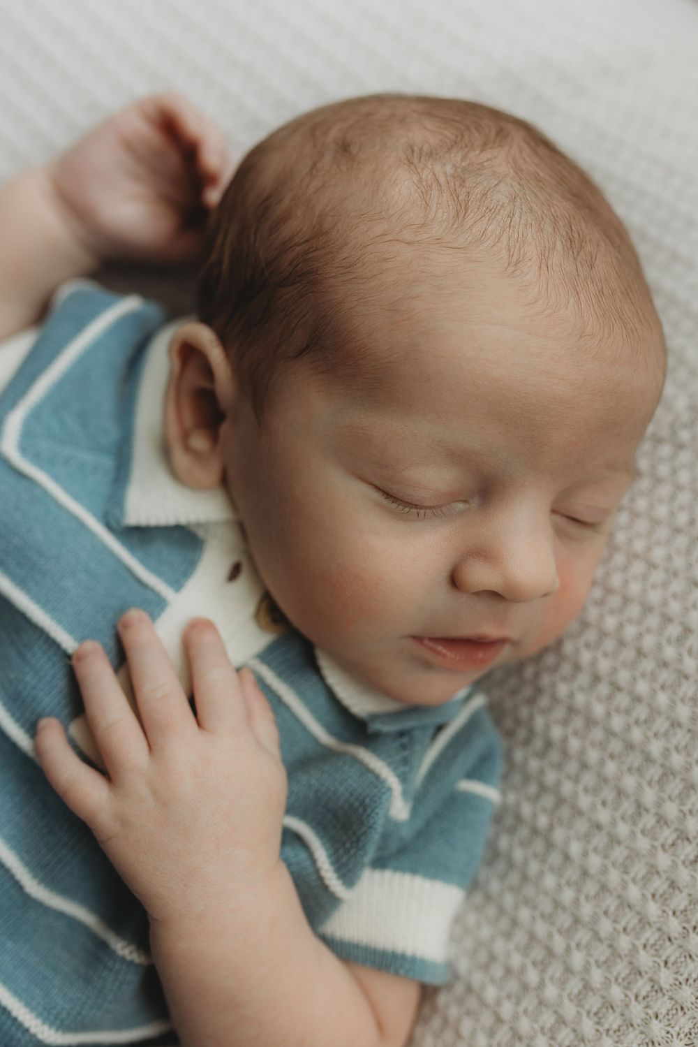 Peaceful newborn baby sleeping in a blue striped outfit on a white knit blanket.
