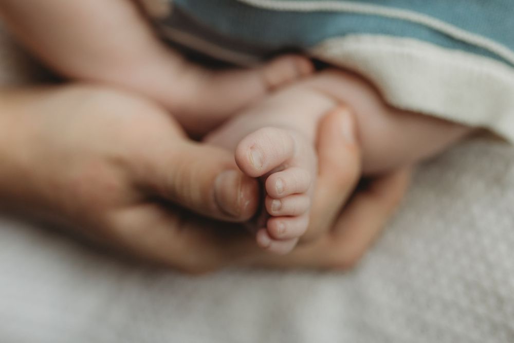 Close-up of a newborn baby's tiny feet cradled gently in an adult's hands on a soft blanket.