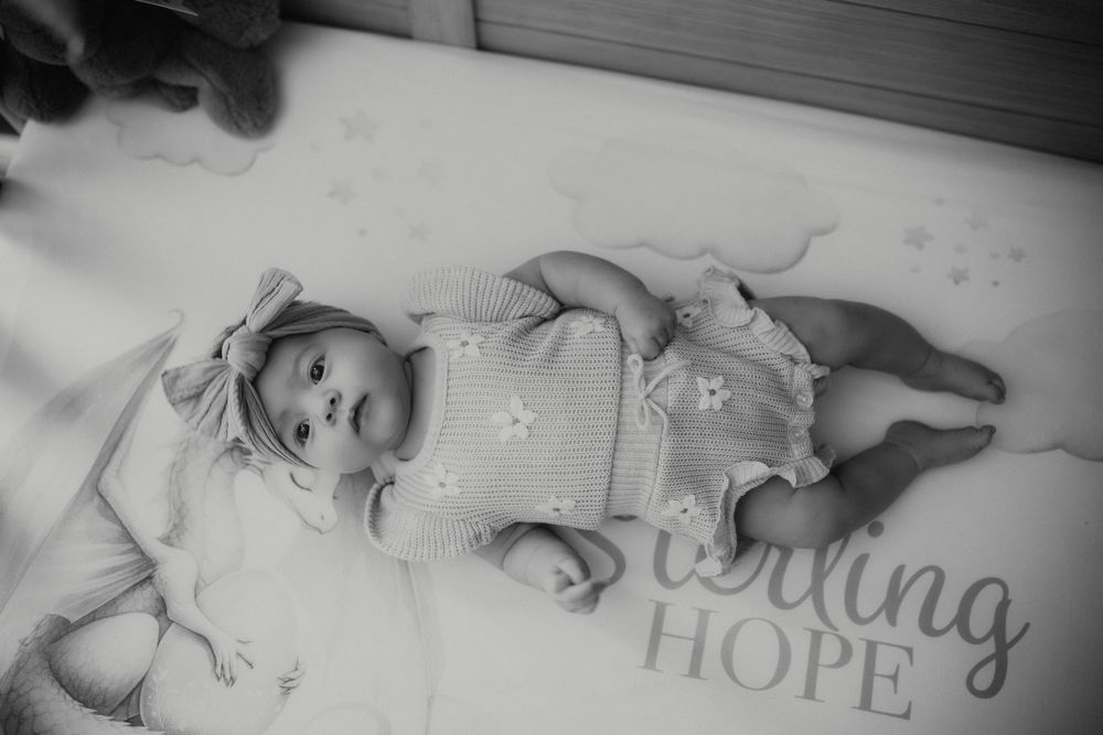 Black and white newborn baby photo lying on blanket with inspiring Hope text, wearing floral romper and bow headband.