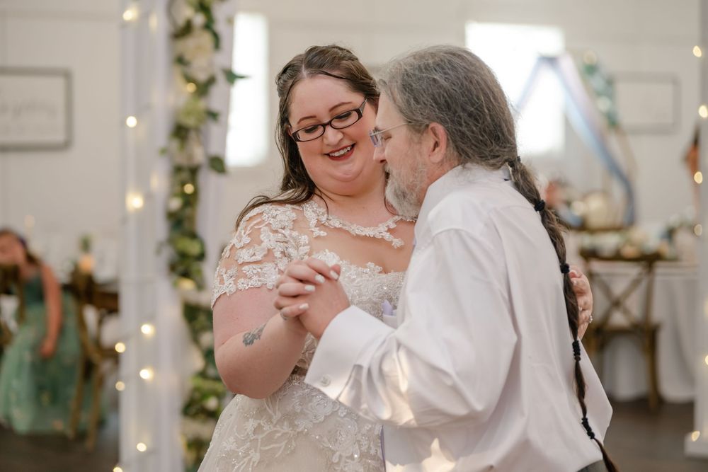 Bride and groom share their first dance, smiling joyfully at a wedding reception with fairy lights and floral decor.