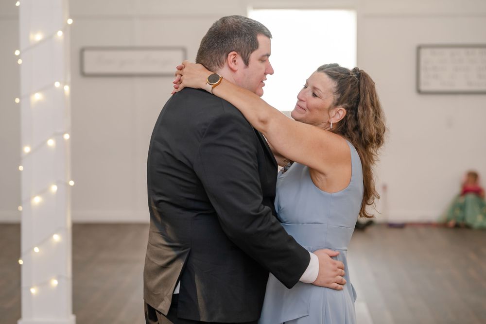 Couple sharing a romantic dance in a white decorated venue, man in black suit and woman in blue gown.