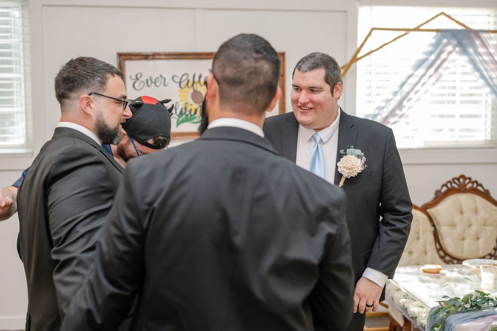 Groomsmen in black suits socializing and laughing together at a wedding reception venue.