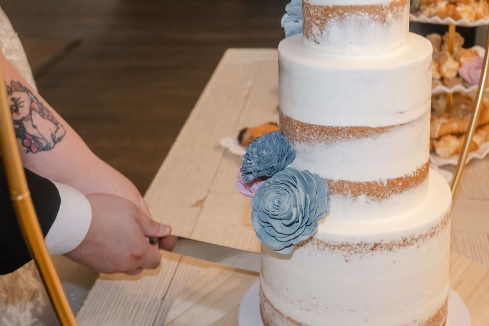 Bride and groom cutting a elegant three-tier white wedding cake decorated with blue flowers.