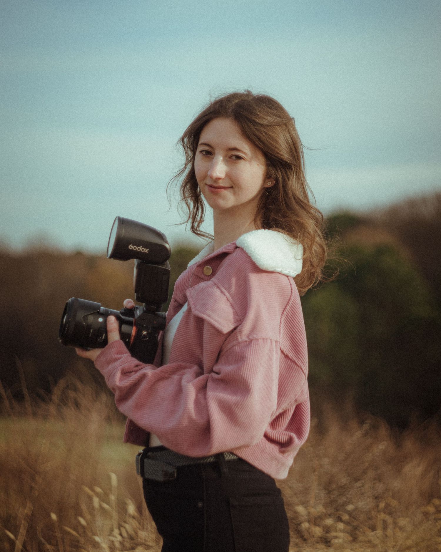 A photographer holds professional camera equipment in a field during golden hour.