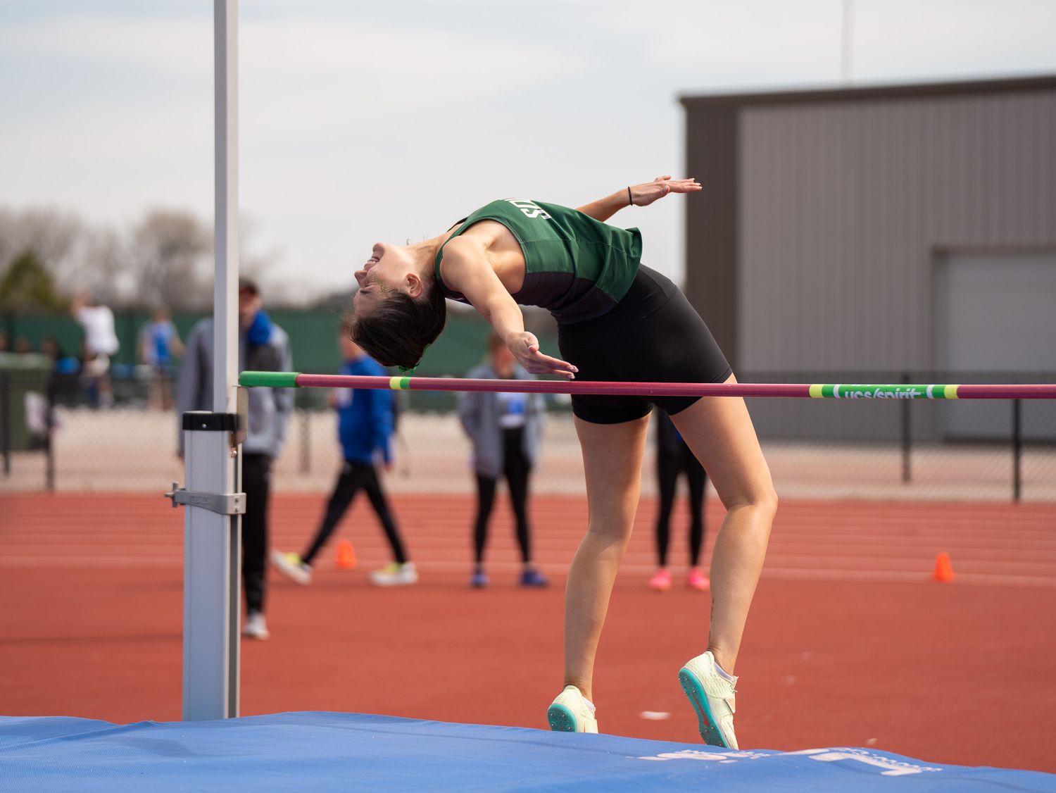 High jumper in green uniform arches over bar during competition.
