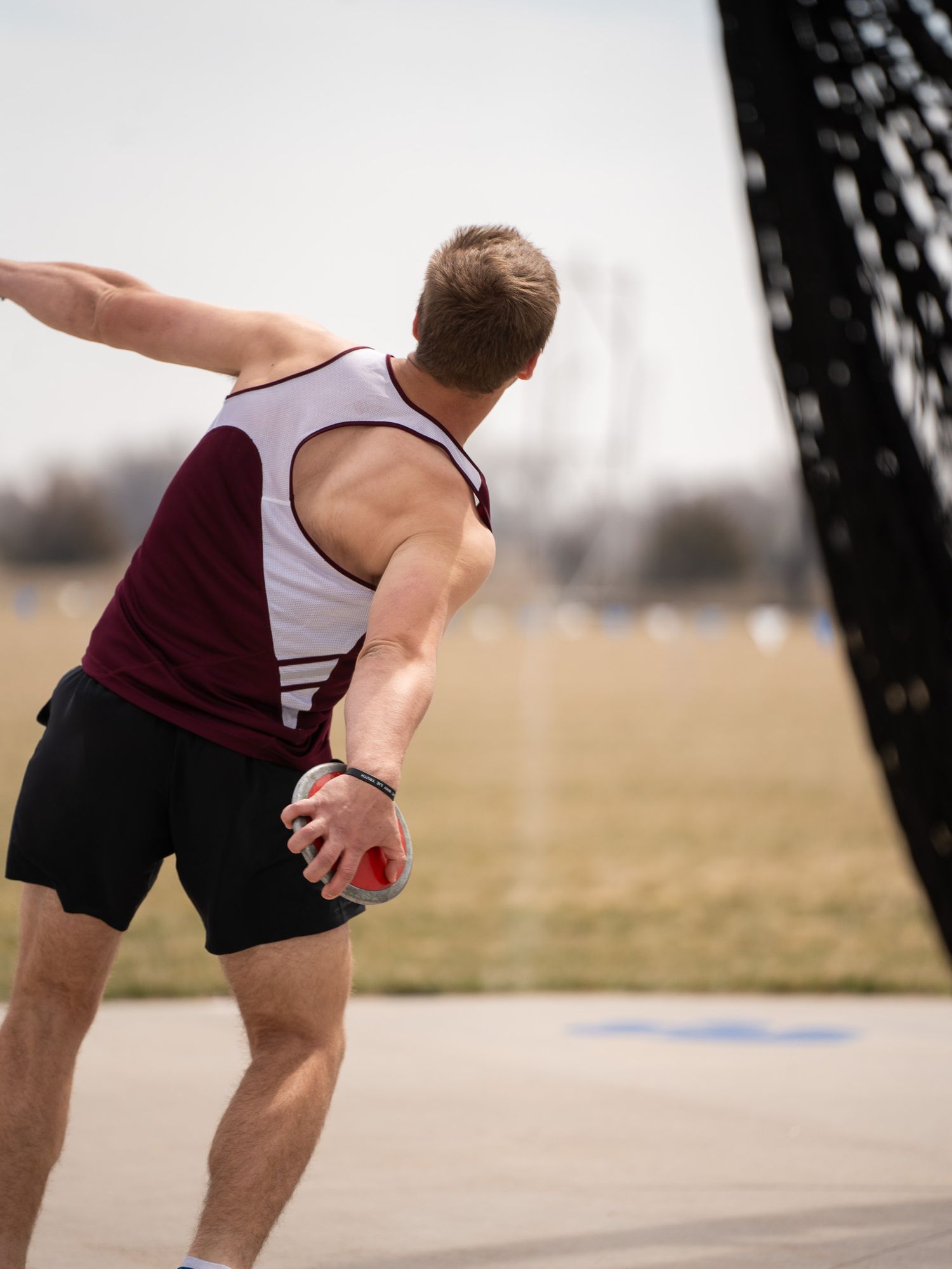 Track athlete in sleeveless uniform winds up for discus throw.